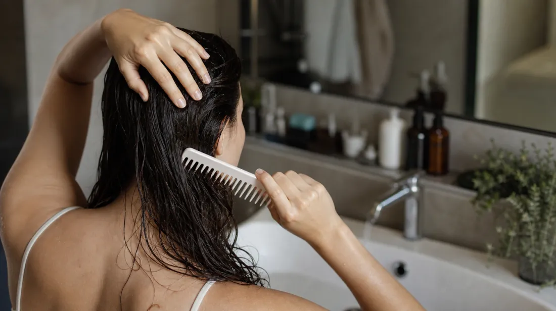 Woman combing wet hair with a wide-tooth comb, holding hair near the roots